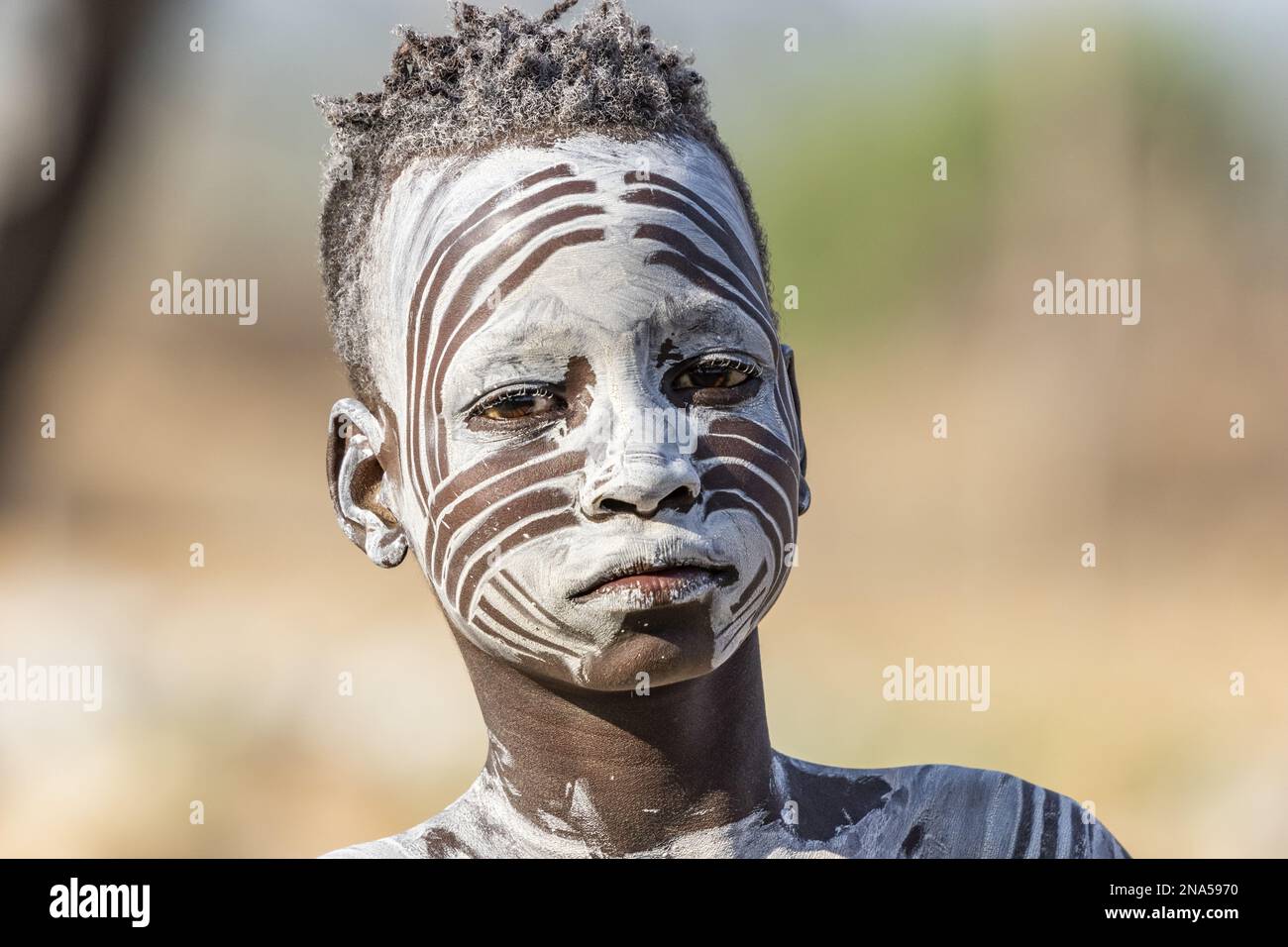 Young Karo man getting his face decorated with traditional face paint at Kortcho Village; Omo Valley, Ethiopia Stock Photo