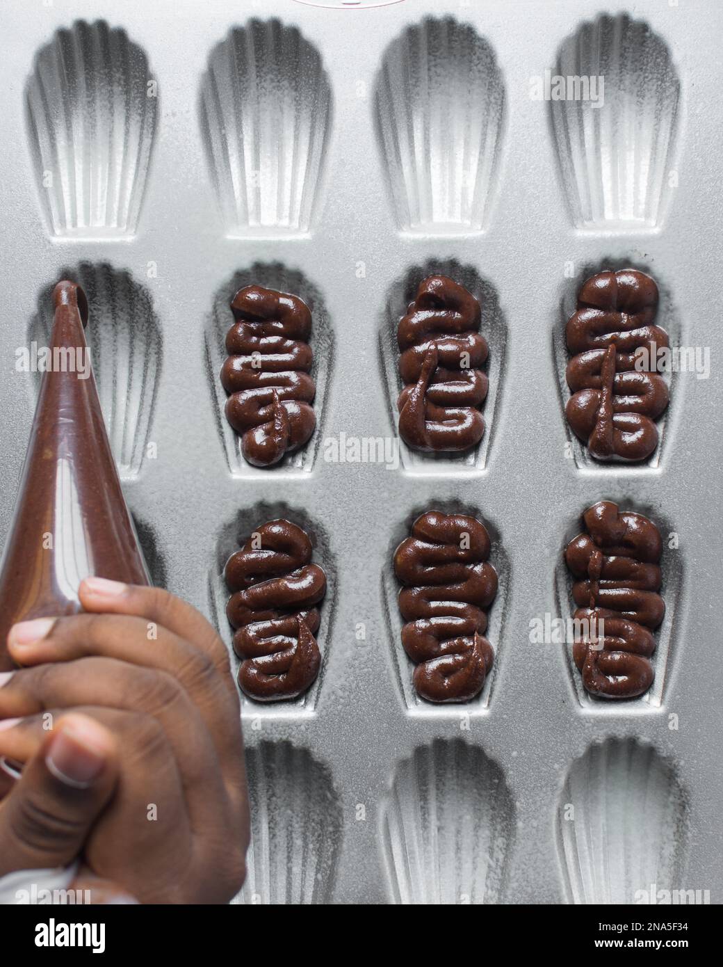 Piping chocolate Madeleine batter into a greased Madeleine pan