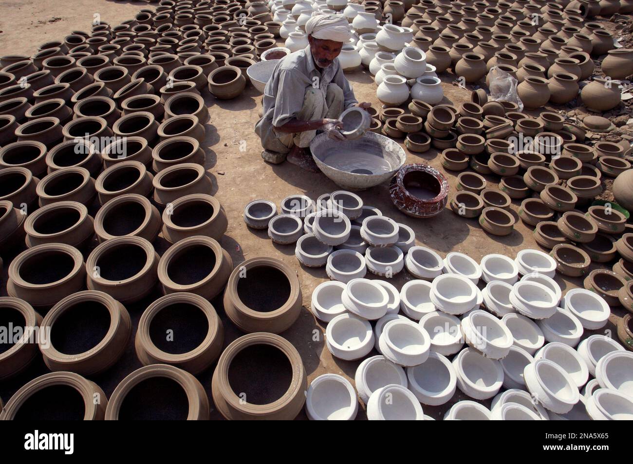 A Pakistani potter applies color to clay pots at his in Lahore