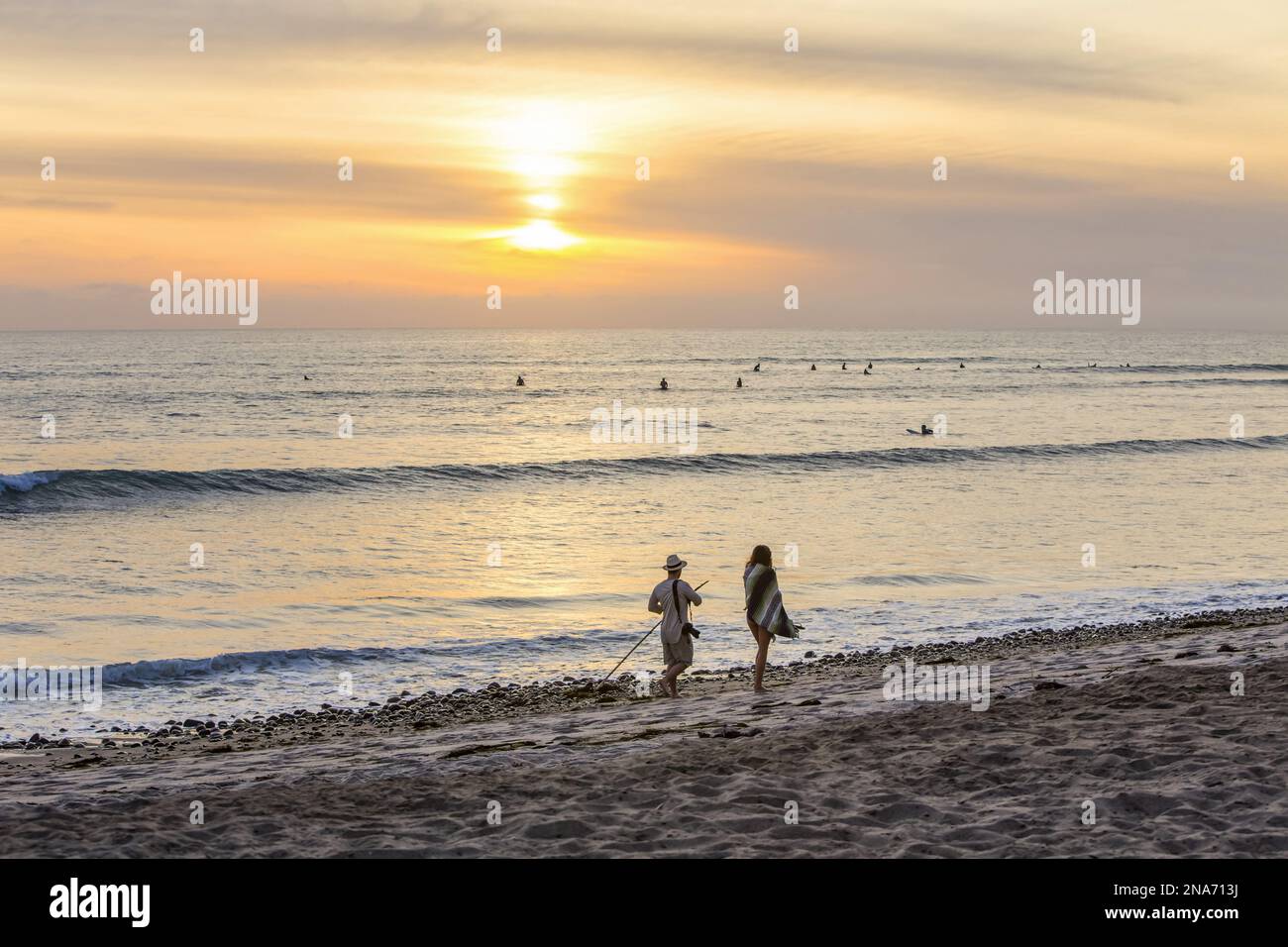 Surfers in the water and people walking the beach at sunset, San Onofre State Beach; San Clemente, California, United States Stock Photo