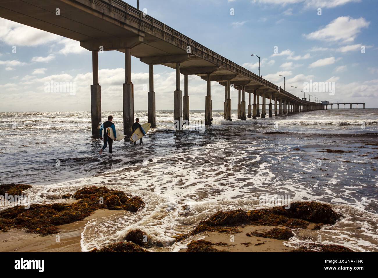 Surfers walking in the surf from a beach under an elevated roadway in San Diego; San Diego, California, United States of America Stock Photo