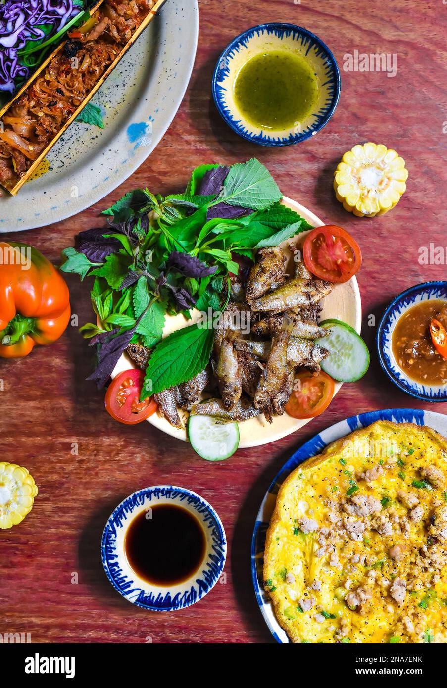 Vietnamese cuisine set made of braised deer in bamboo, fried fish, omelette with sauces on wooden table Stock Photo