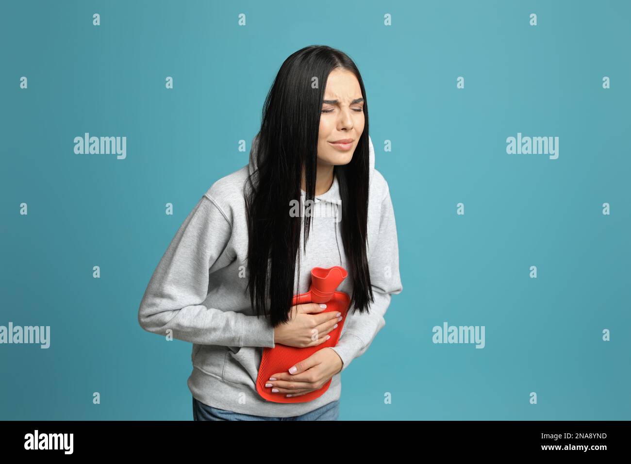 Woman using hot water bottle to relieve abdominal pain on light blue