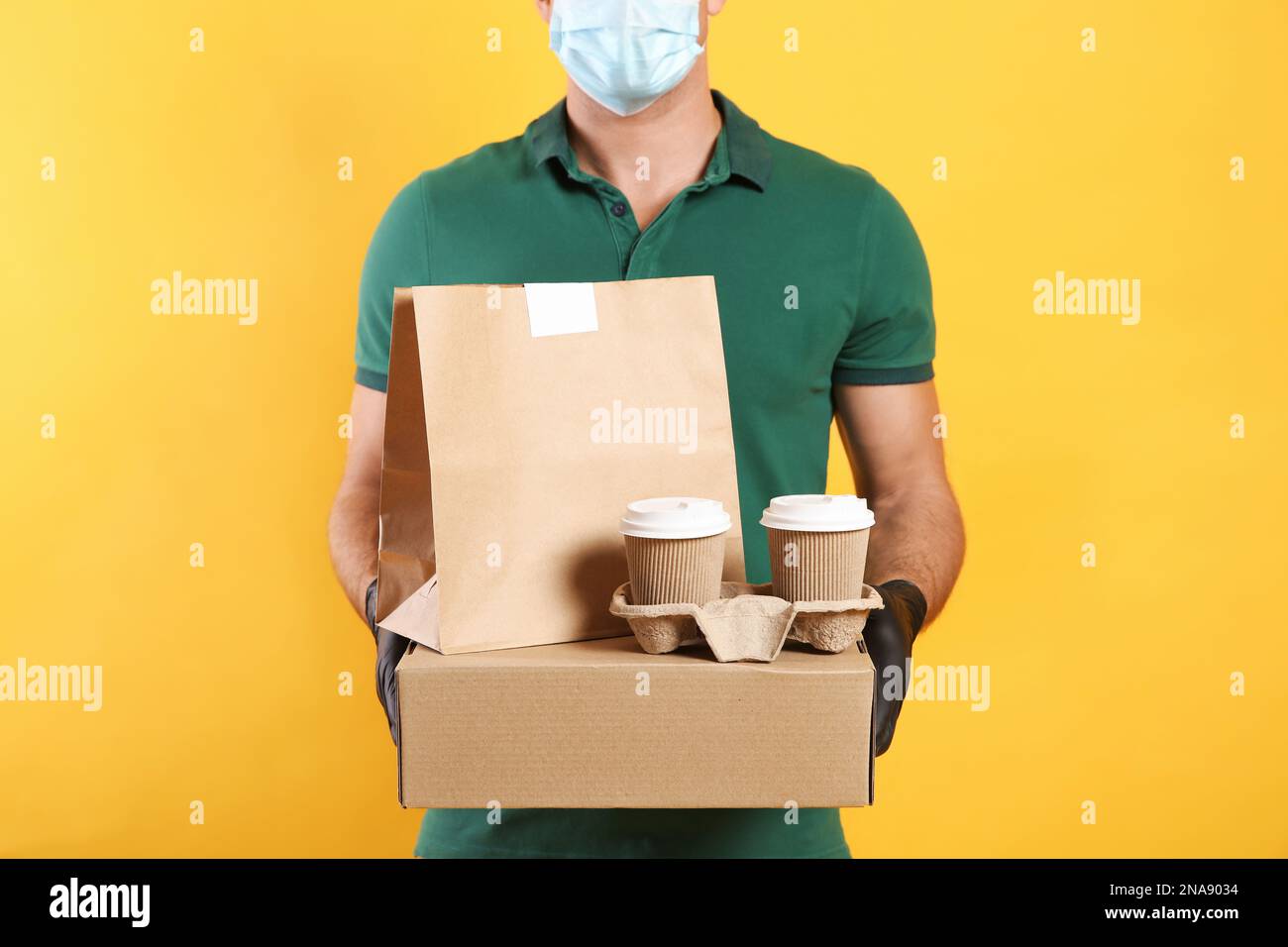 Delivery man in gloves and mask holds box on yellow background