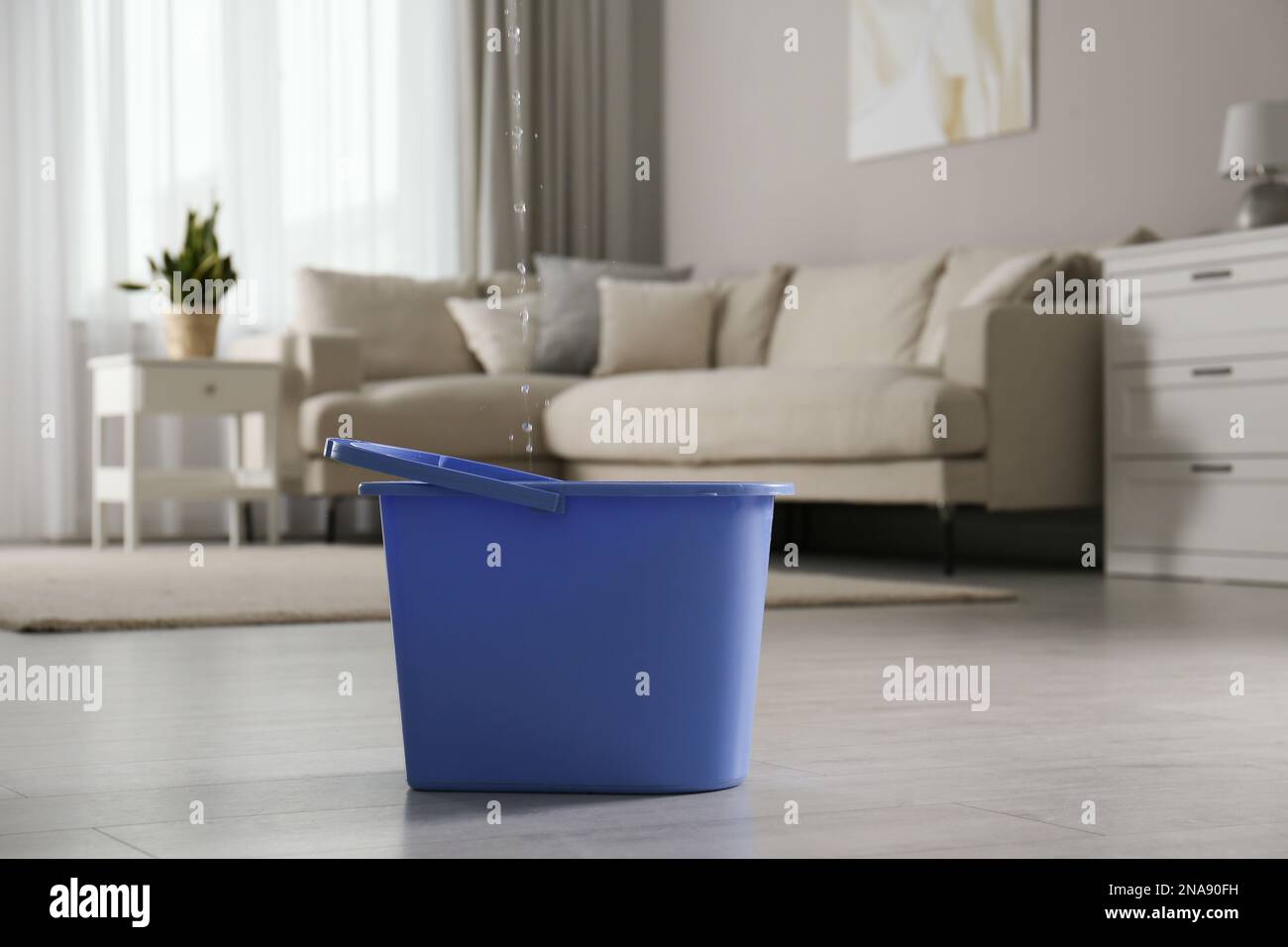 Water dripping from ceiling into plastic bucket on floor in living room