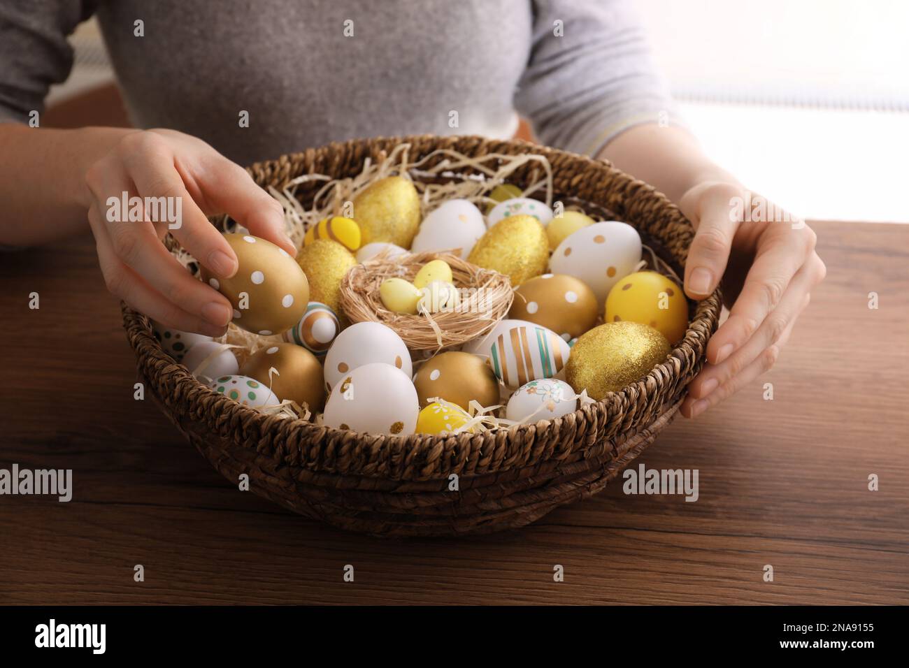 Woman with basket full of dyed Easter eggs at wooden table, closeup. Easter celebration Stock Photo