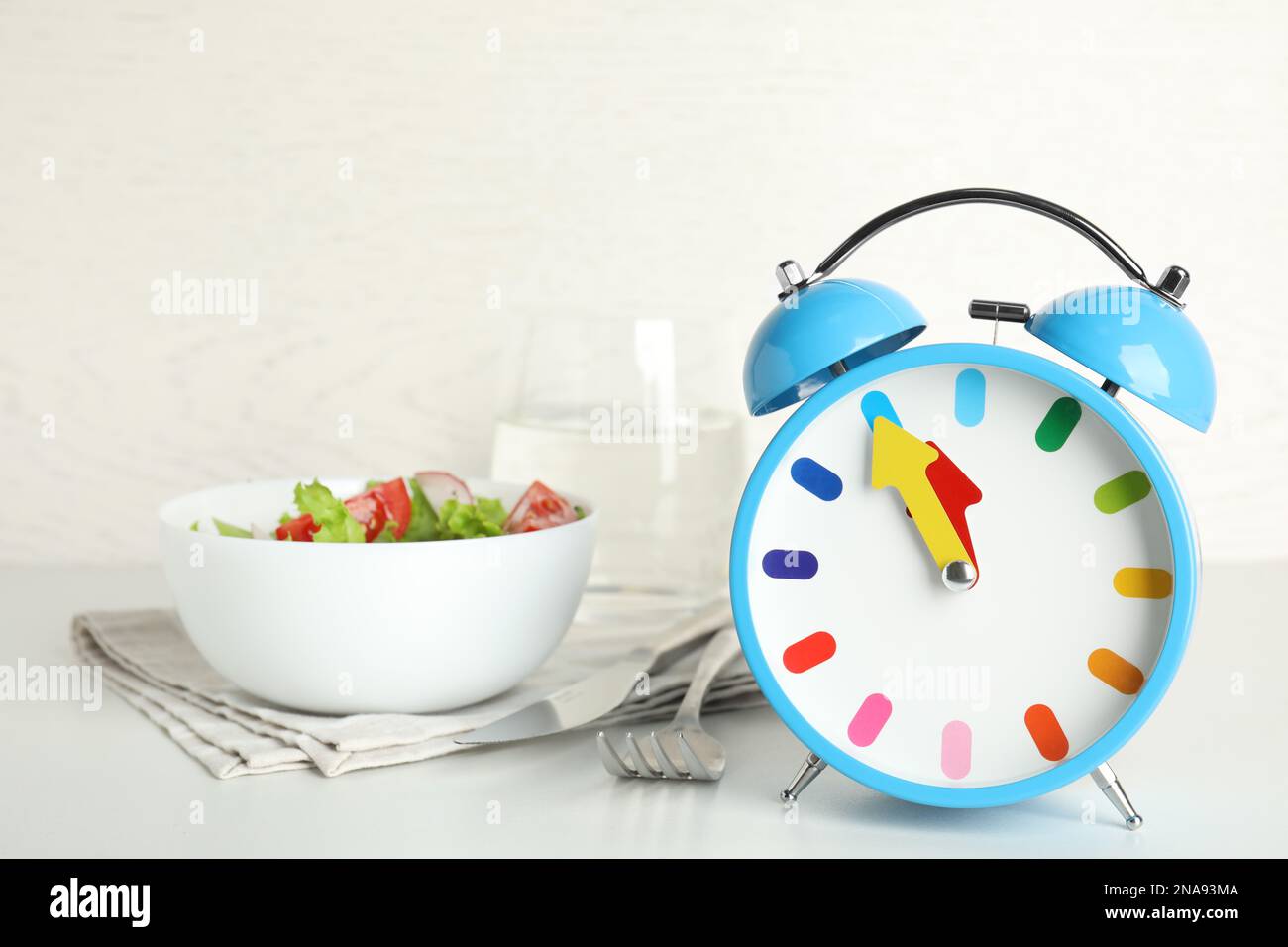 Alarm clock with salad on white table. Meal timing concept Stock Photo