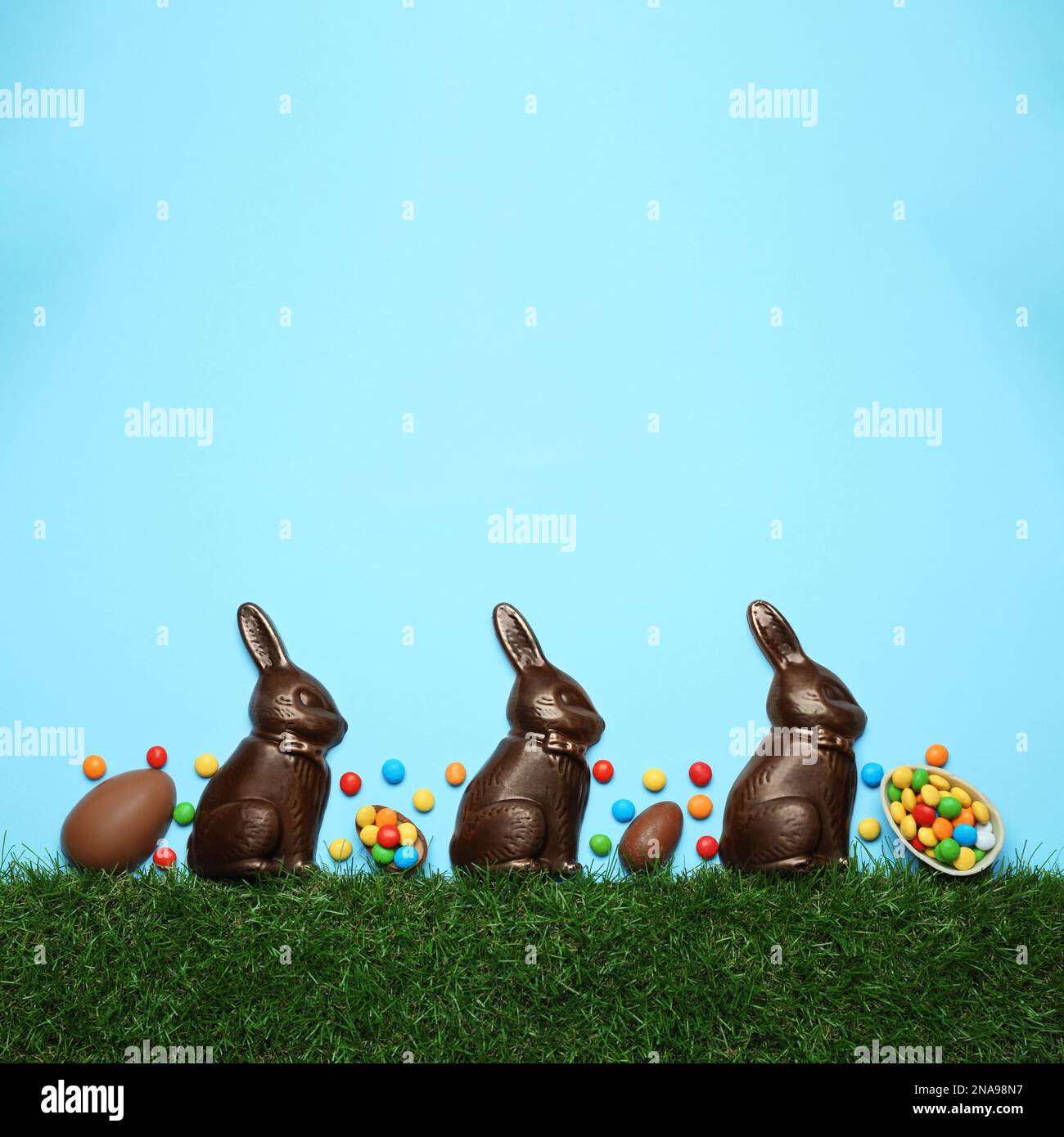 Chocolate Easter bunnies, eggs and candies with green grass on light