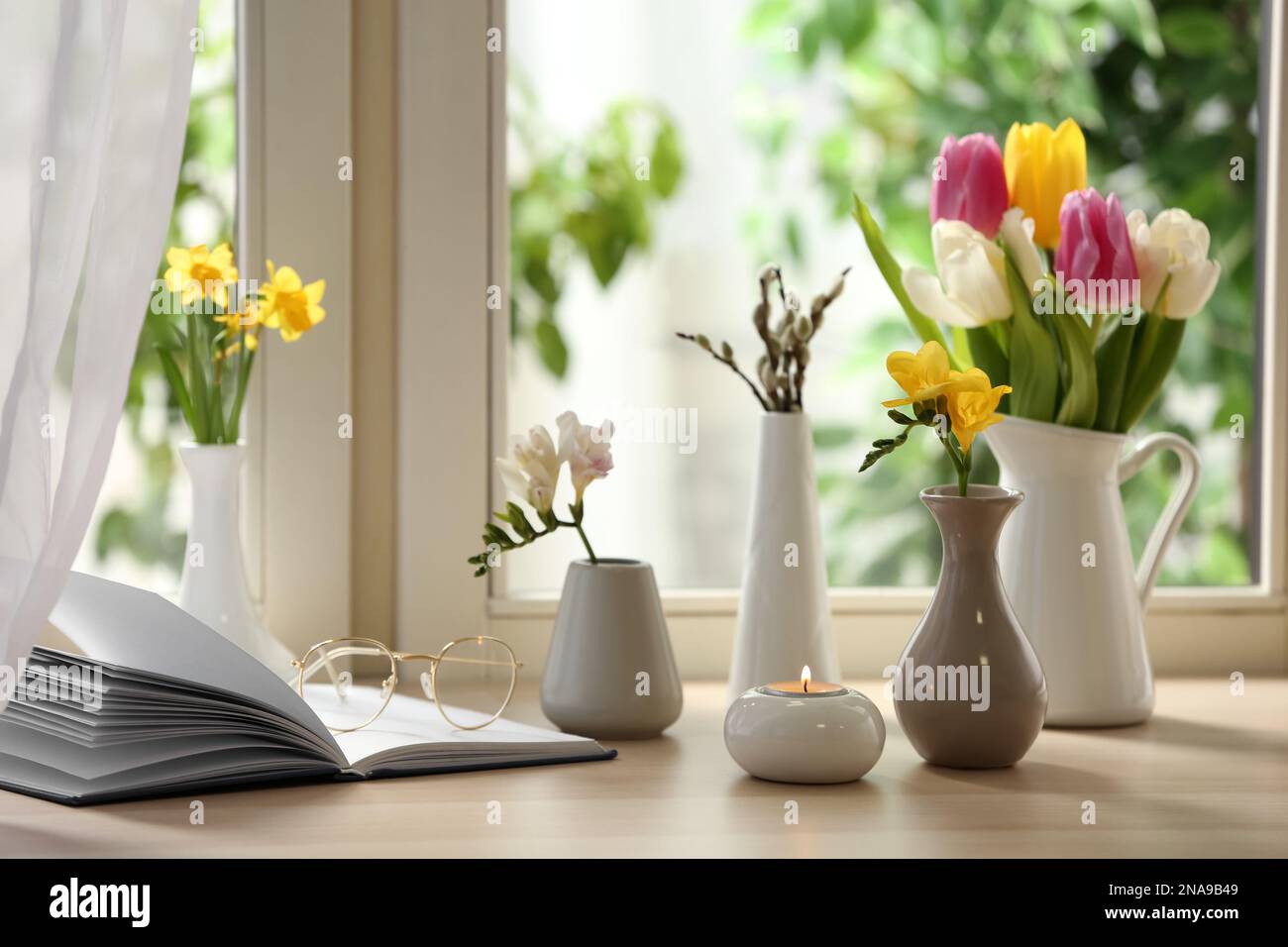 Different beautiful spring flowers, burning candle and book on window ...