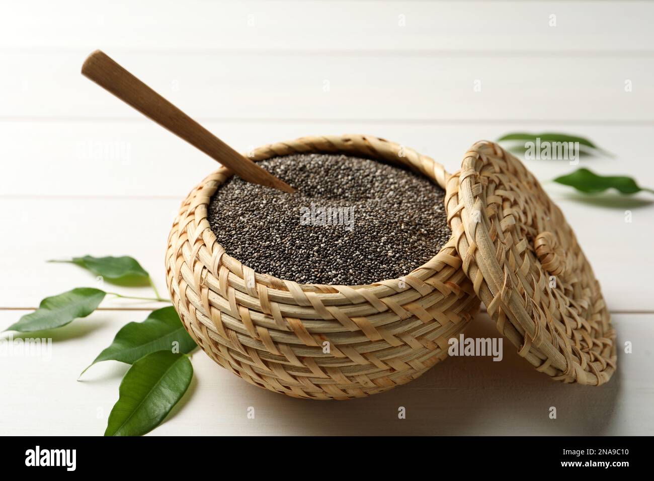 Wicker box with chia seeds and spoon on white wooden table Stock Photo
