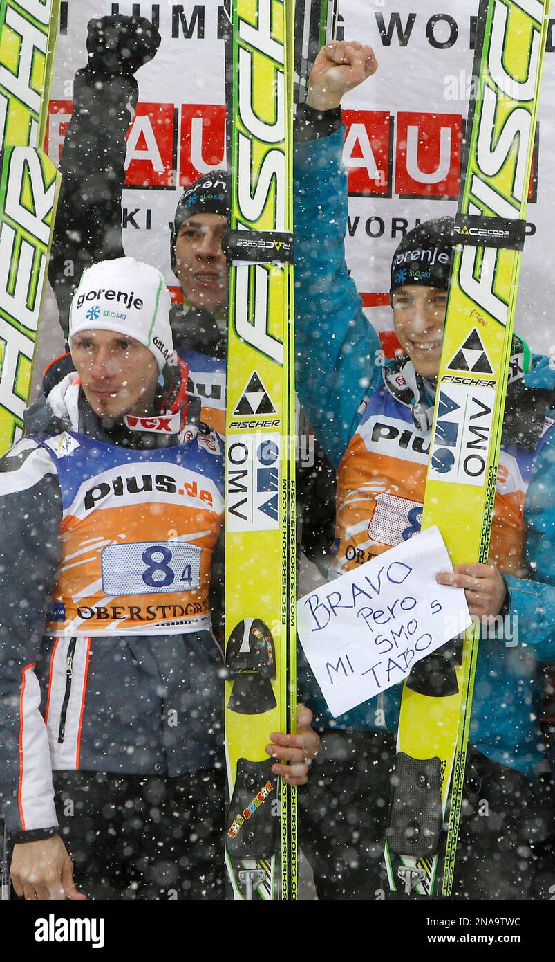 Slovenia's Robert Kranjec, foreground left, Jure Sinkovec, rear, and Juri Tepec hold a sign that reads "Thank you Pero-We are with you" after winning the ski flying World Cup in Oberstdorf, southern Germany, on Sunday, Feb. 19, 2012. Team mate Peter Prevc, not pictured, crashed during his jump. (AP Photo/Matthias Schrader) Stock Photo