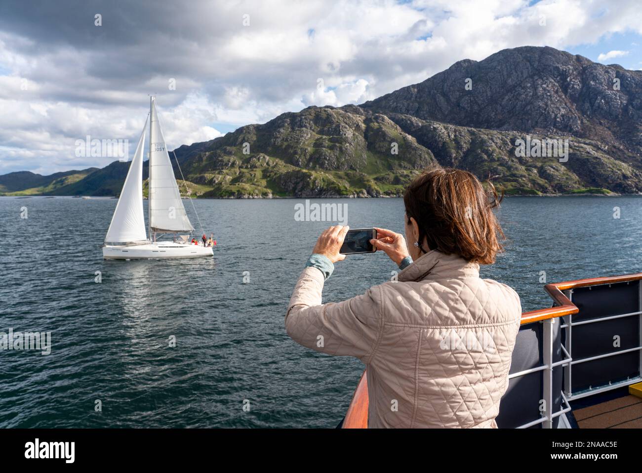 A guest aboard a tour boat photographs a sailboat near Inverie, Scotland; Inverie, Scotland Stock Photo