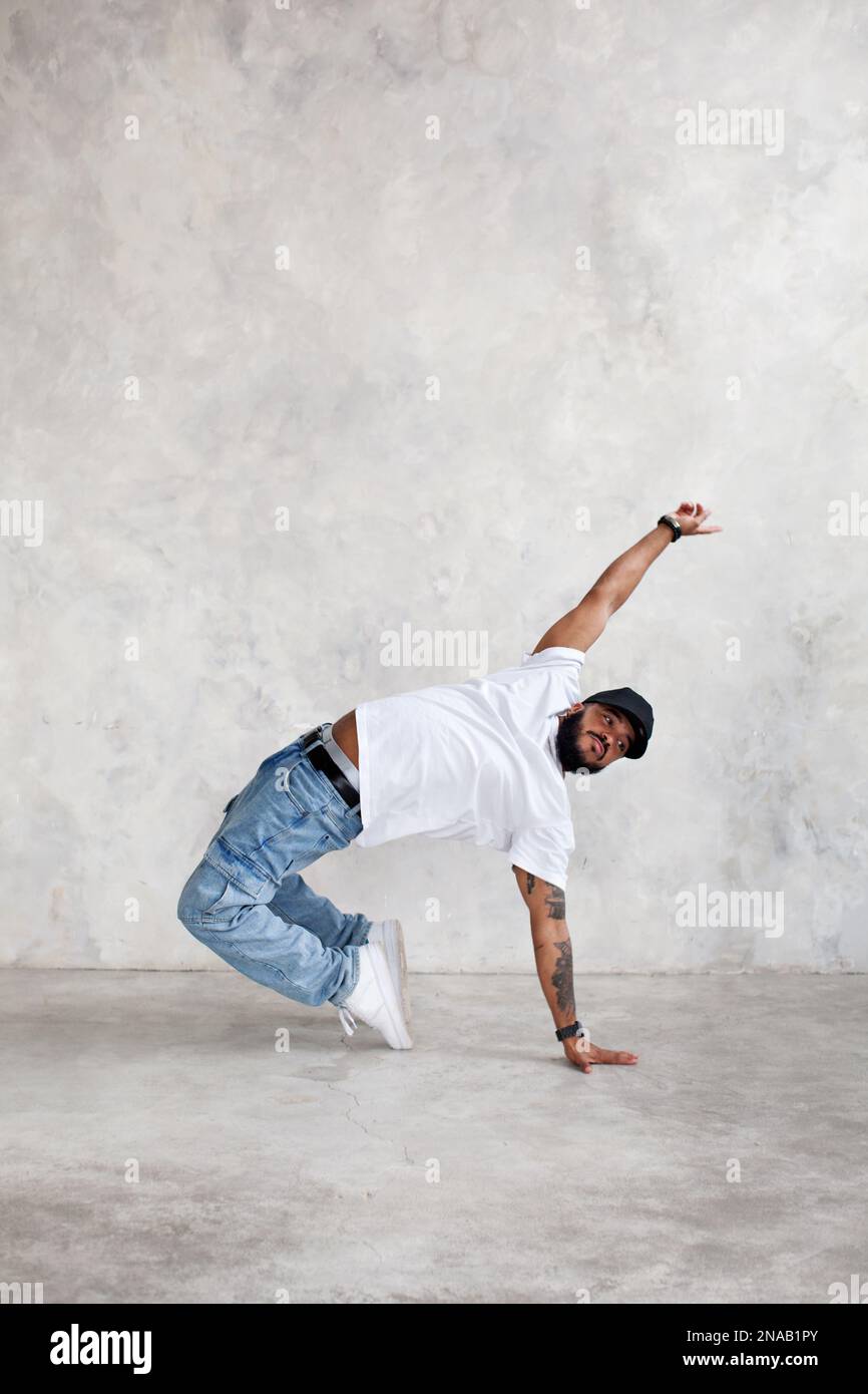 Man dancing break dance against background of gray wall in studio. Cool