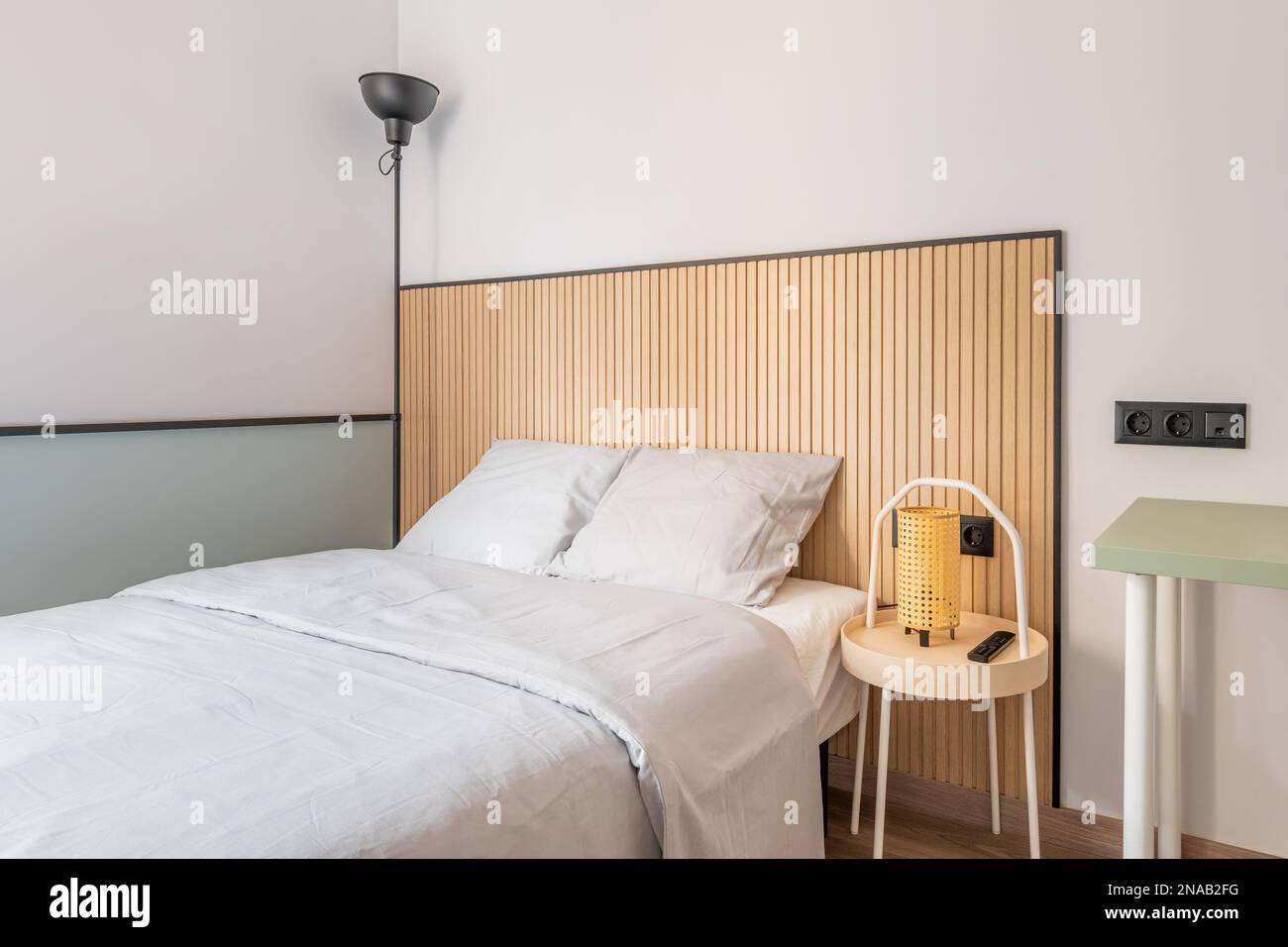 Part of a bedroom with a double bed against a white wall with designer