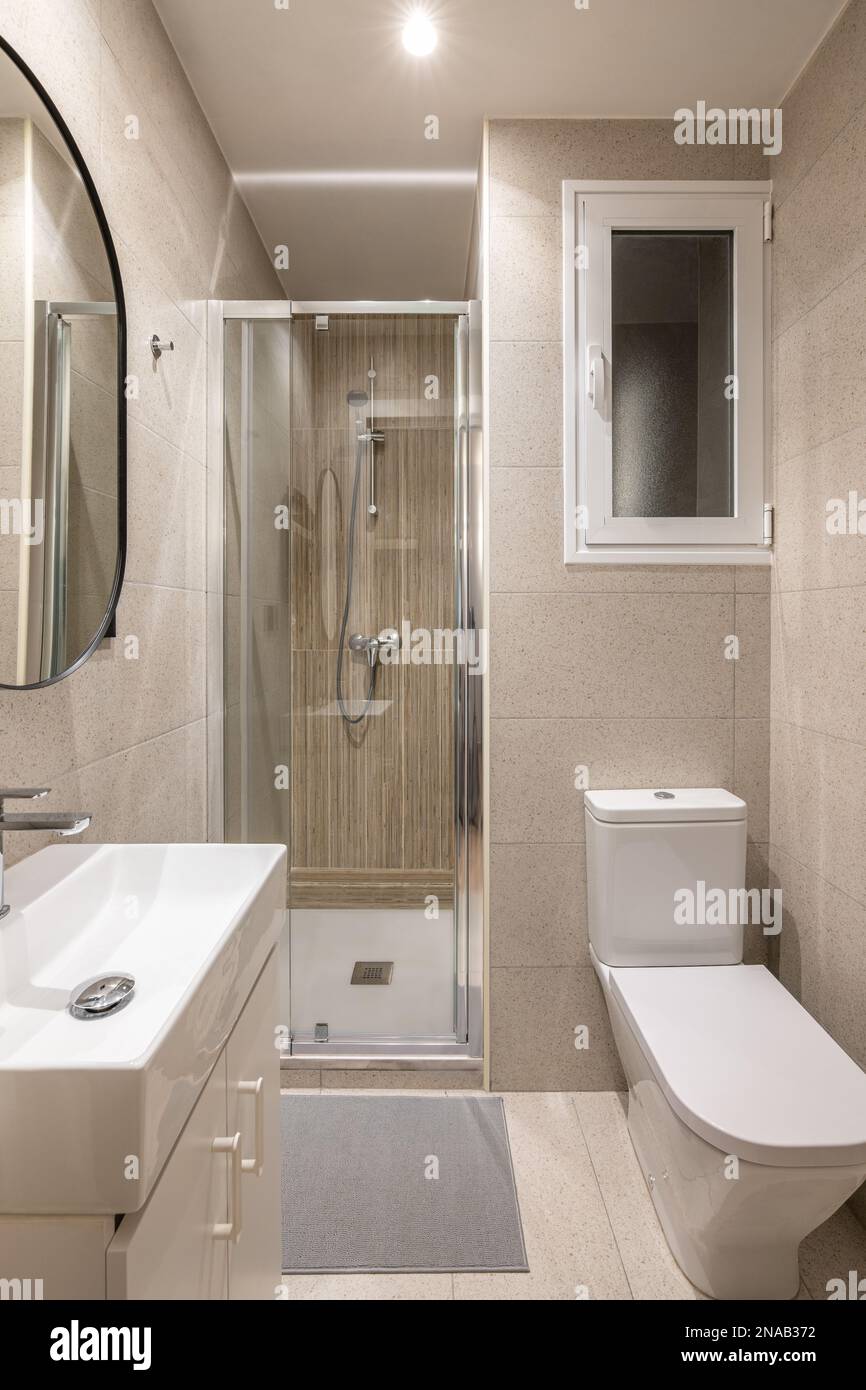 Compact bathroom with bright lighting from ceiling. Beige granite tiles on  walls. White toilet bowl and sink on dressing table, shower area with Stock  Photo - Alamy