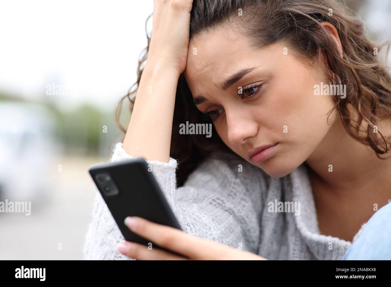 Sad woman checking phone message complaining in the street Stock Photo