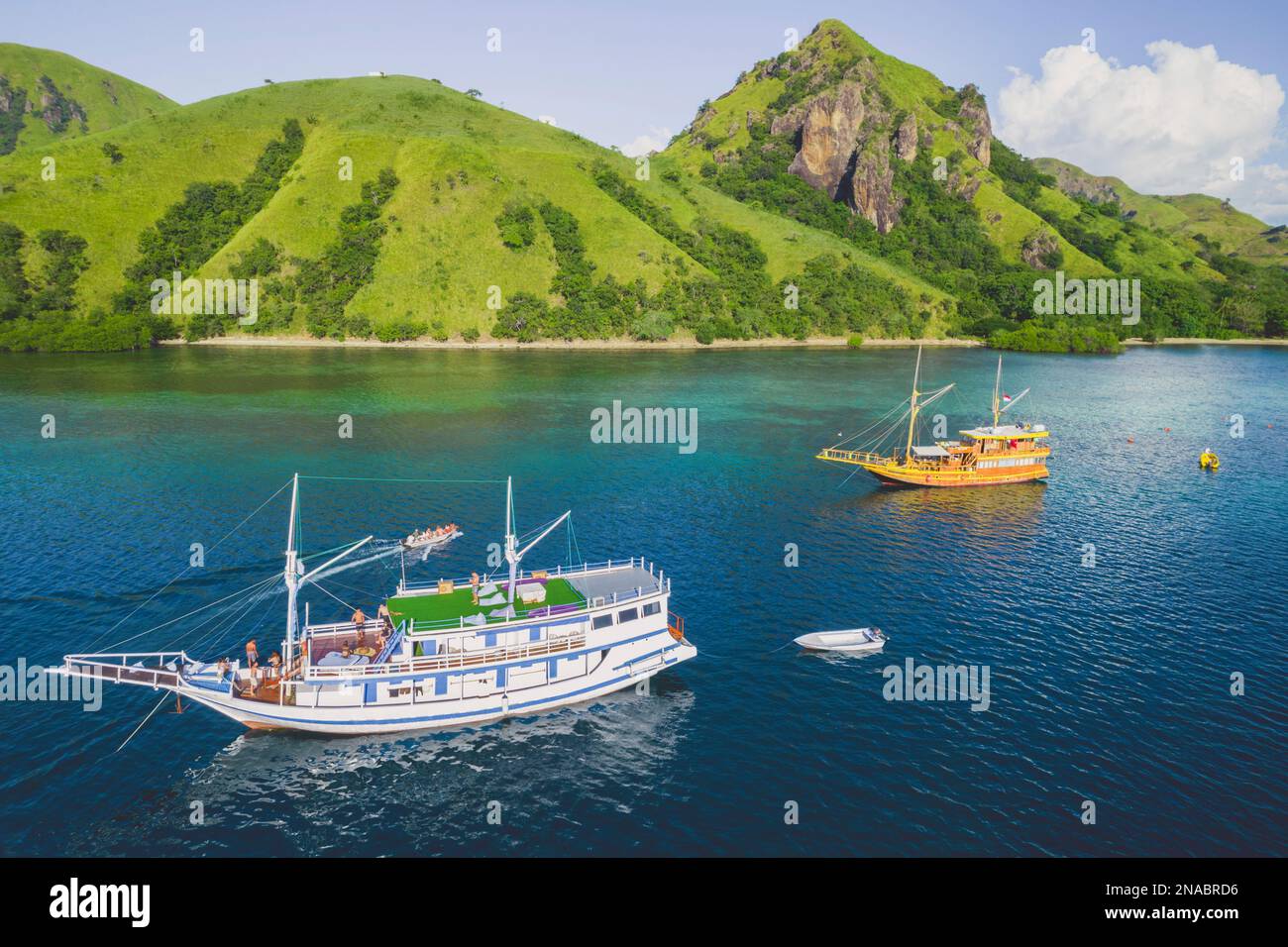 Boats in the tranquil waters along the lush and rugged coastline of Komodo National Park; East Nusa Tenggara, Indonesia Stock Photo