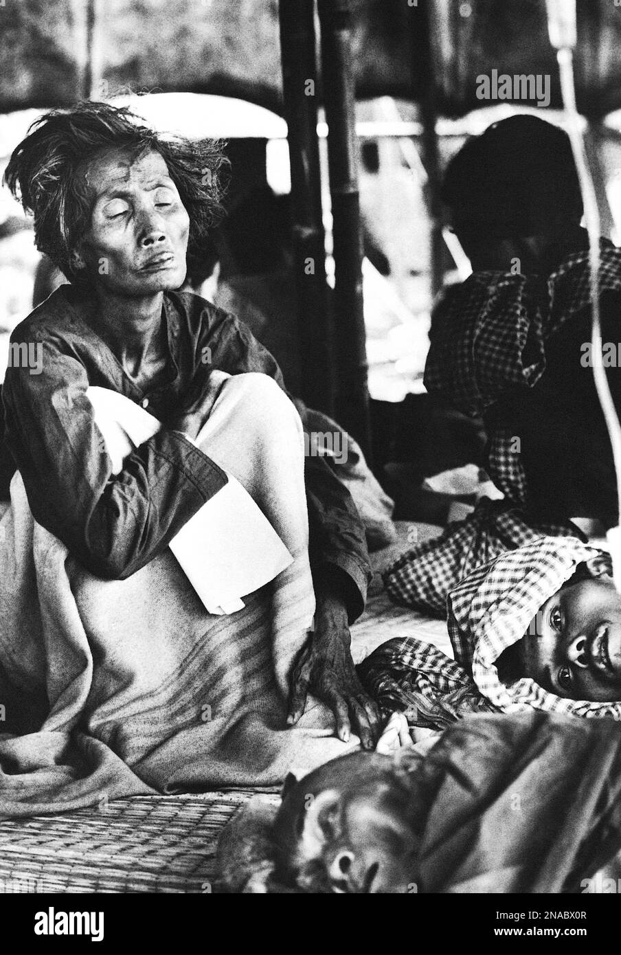 An elderly Cambodian refugee woman sits with her eyes closed, blocking ...