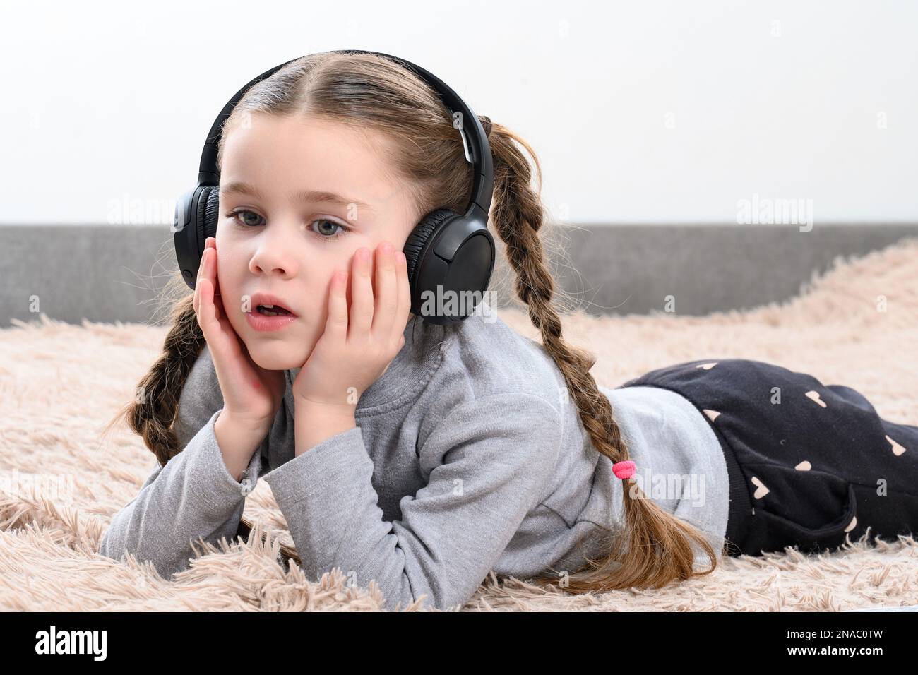 A little girl is lying on the sofa and listening to music in headphones ...