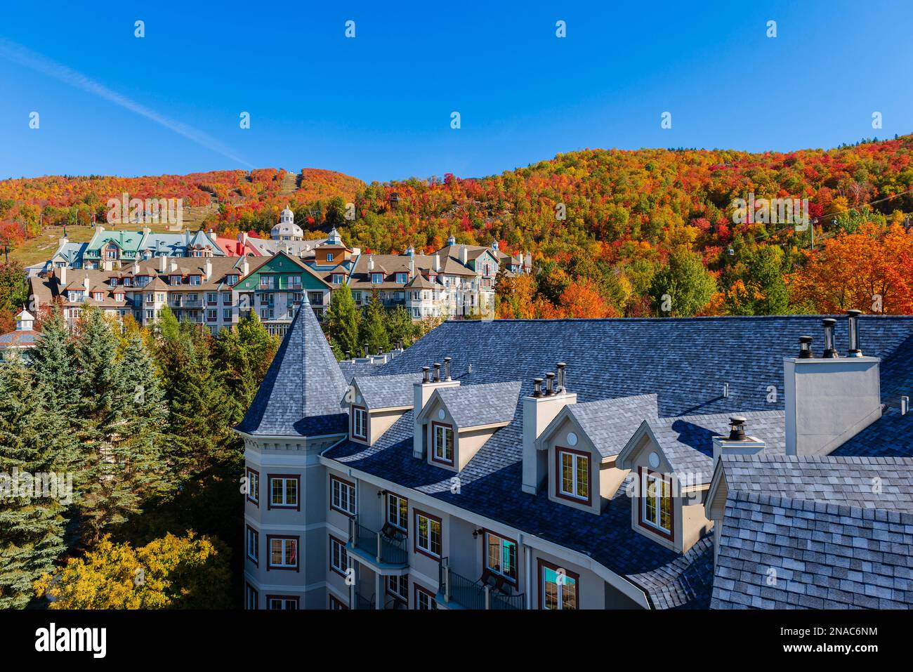 Vibrant autumn colours cover the hills around the residential buildings in the Laurentides of Mont-Tremblant, Quebec;  Mont-Tremblant, Quebec, Canada Stock Photo