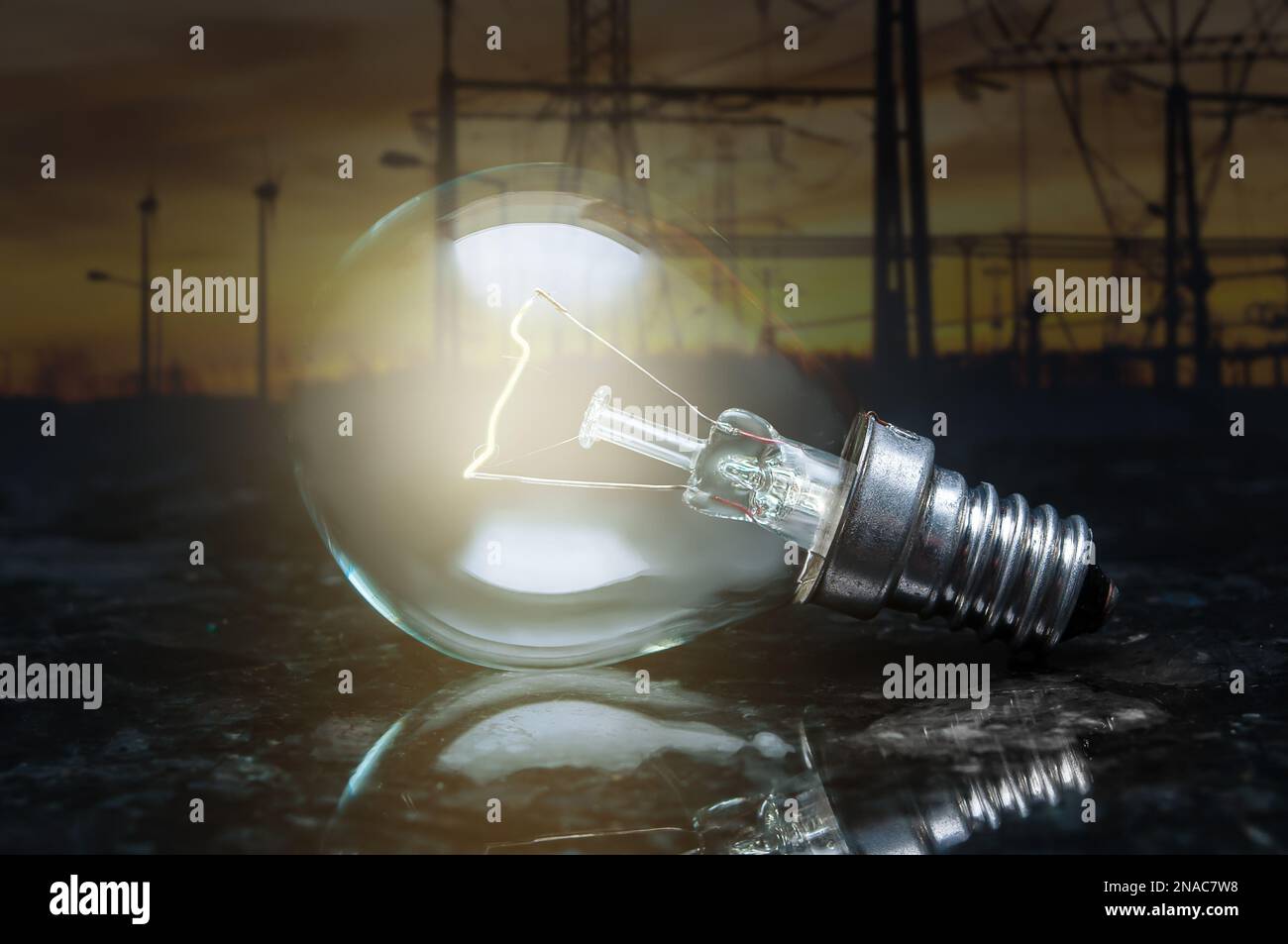 close up of tungsten light bulb with glow on dark polished marble surface and background of high voltage electricity power lines Stock Photo