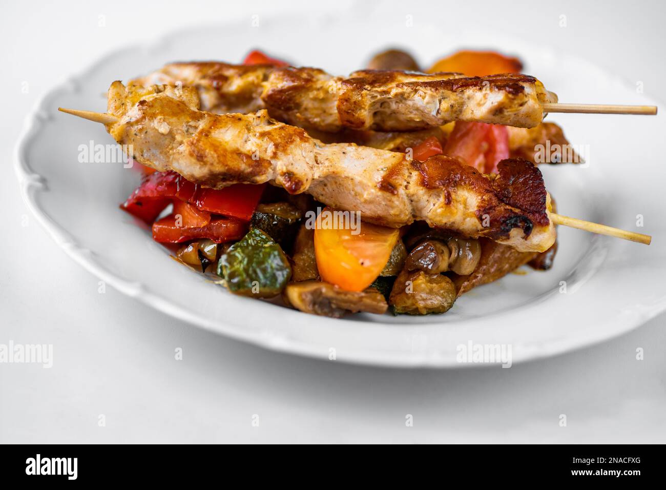 Pork meat on skewer (souvlaki) on baked juicy vegetable. Delicious greek lunch or dinner, closeup. Stock Photo
