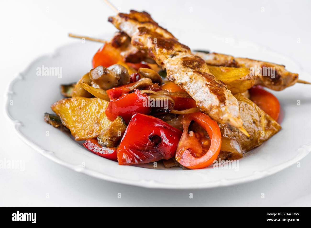 Souvlaki, pork meat on skewer on grilled juicy vegetable on white plate on white background, closeup. Stock Photo