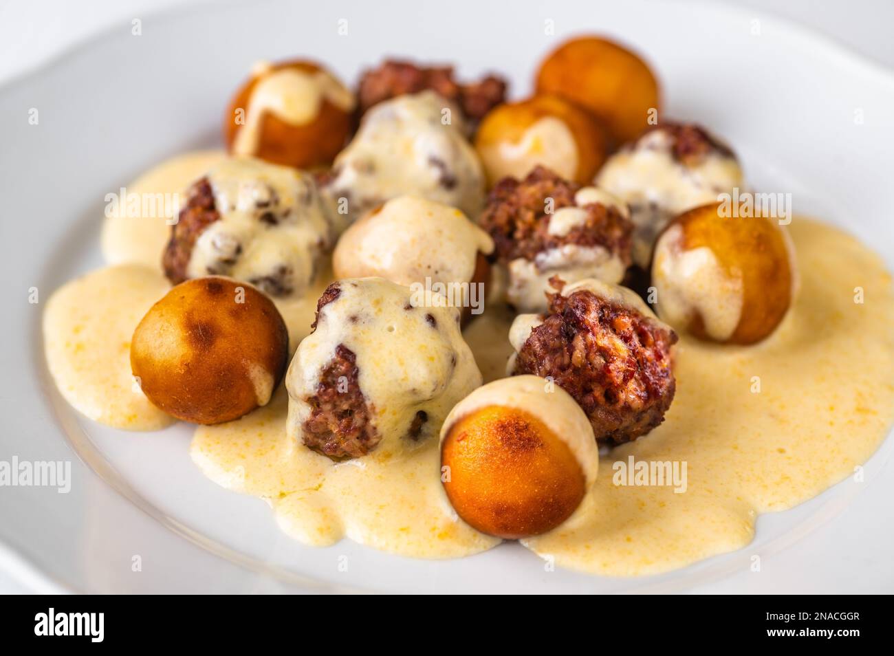 Baked meatball with fried croquette in lemon cheese sauce in white plate, closeup. Stock Photo