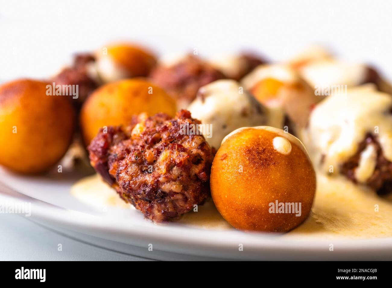 Baked meatball with fried croquette in cheese lemon sauce on white plate, closeup. Stock Photo
