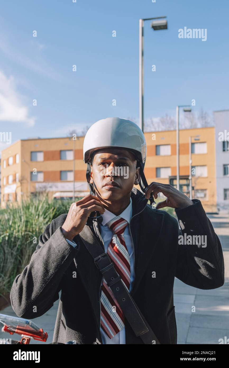 Young businessman putting on helmet riding an electric scooter Stock