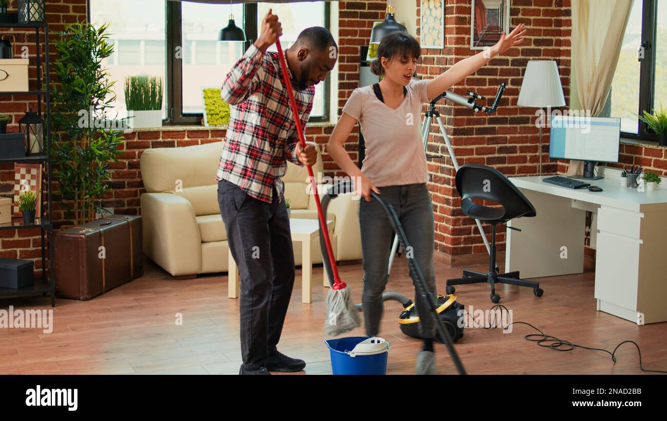 Cheerful people showing dance moves and having fun cleaning living room