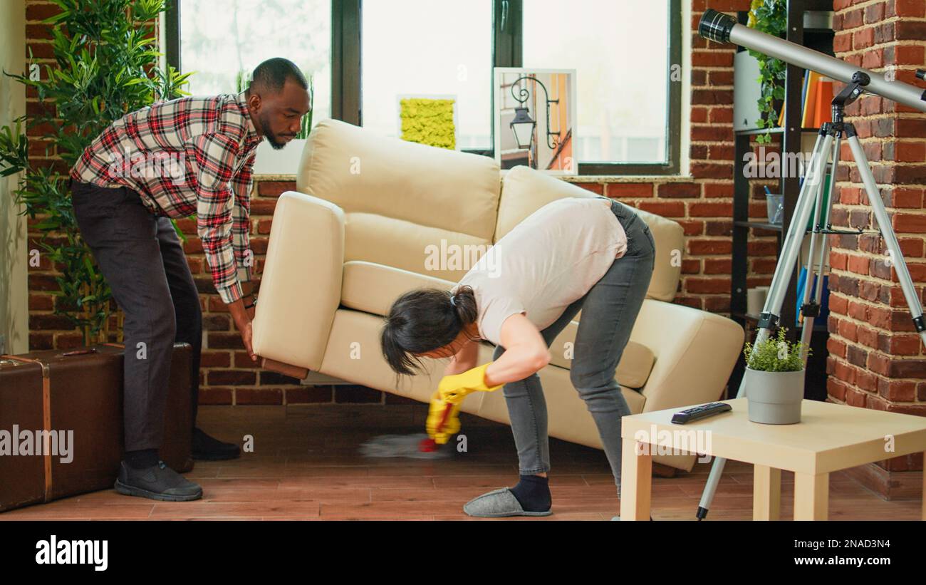 Young couple washing wooden floor with mop, husband helping wife to