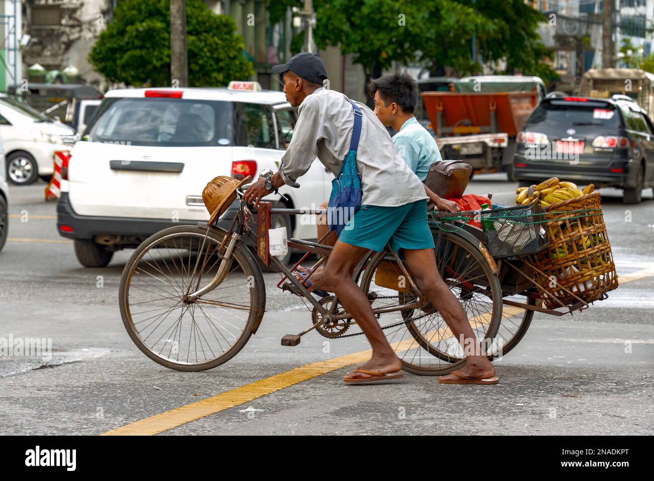 China Town, Yangon - Oct 21, 2017: A tricycle taxi driver carefully pushes his tricycle loaded with a basket full of bananas and a passenger. Stock Photo