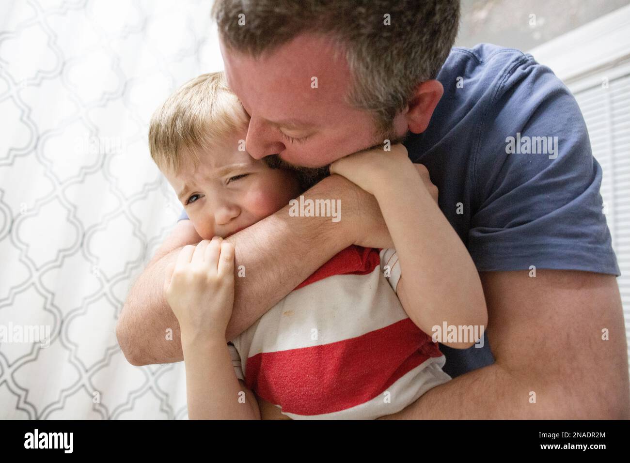 Dad Kisses the Cheek of Upset Son During Bedtime Routine Stock Photo