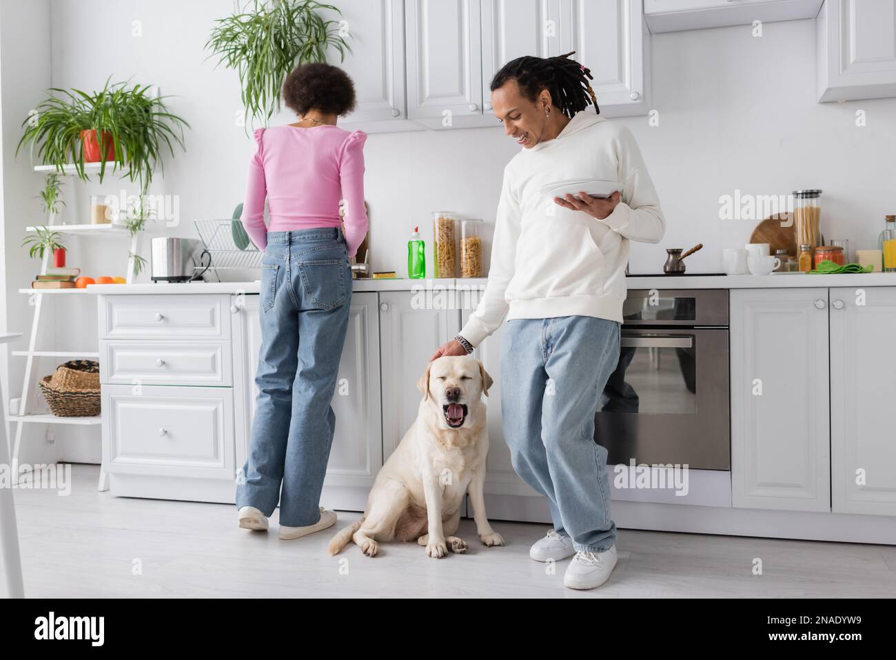African american woman washing dishes near boyfriend petting labrador