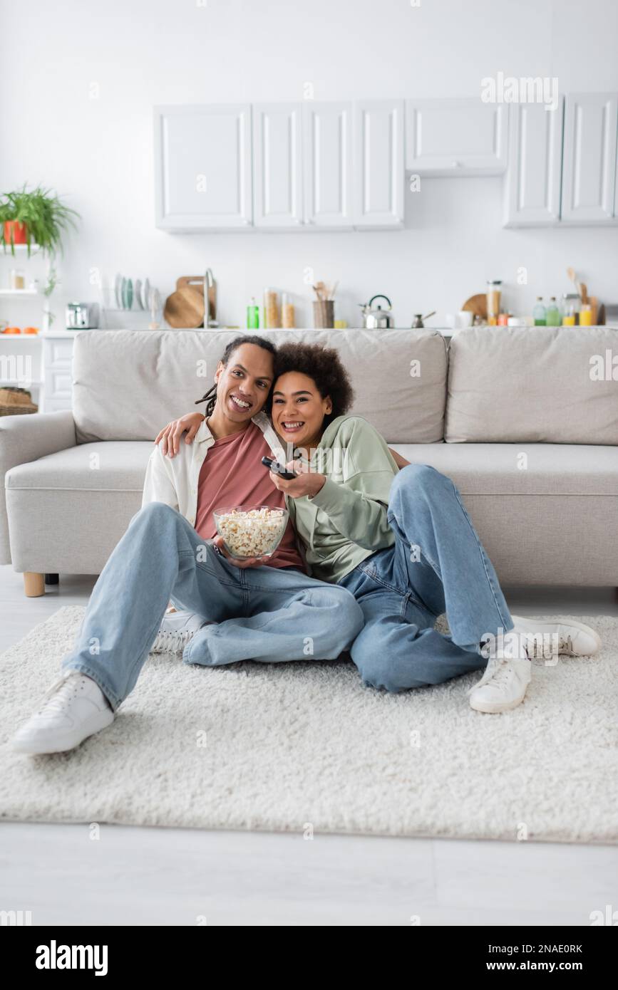 Smiling african american woman hugging boyfriend with popcorn while ...