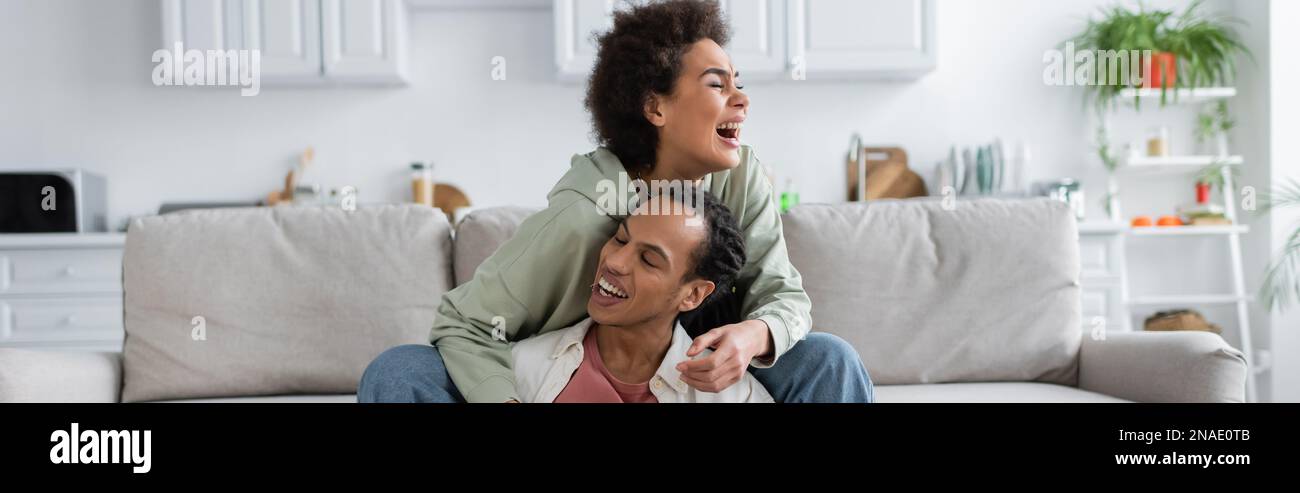 Excited african american woman hugging boyfriend while siting on couch ...