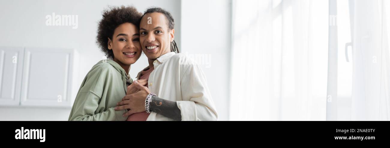 African american couple hugging and looking at camera in kitchen ...