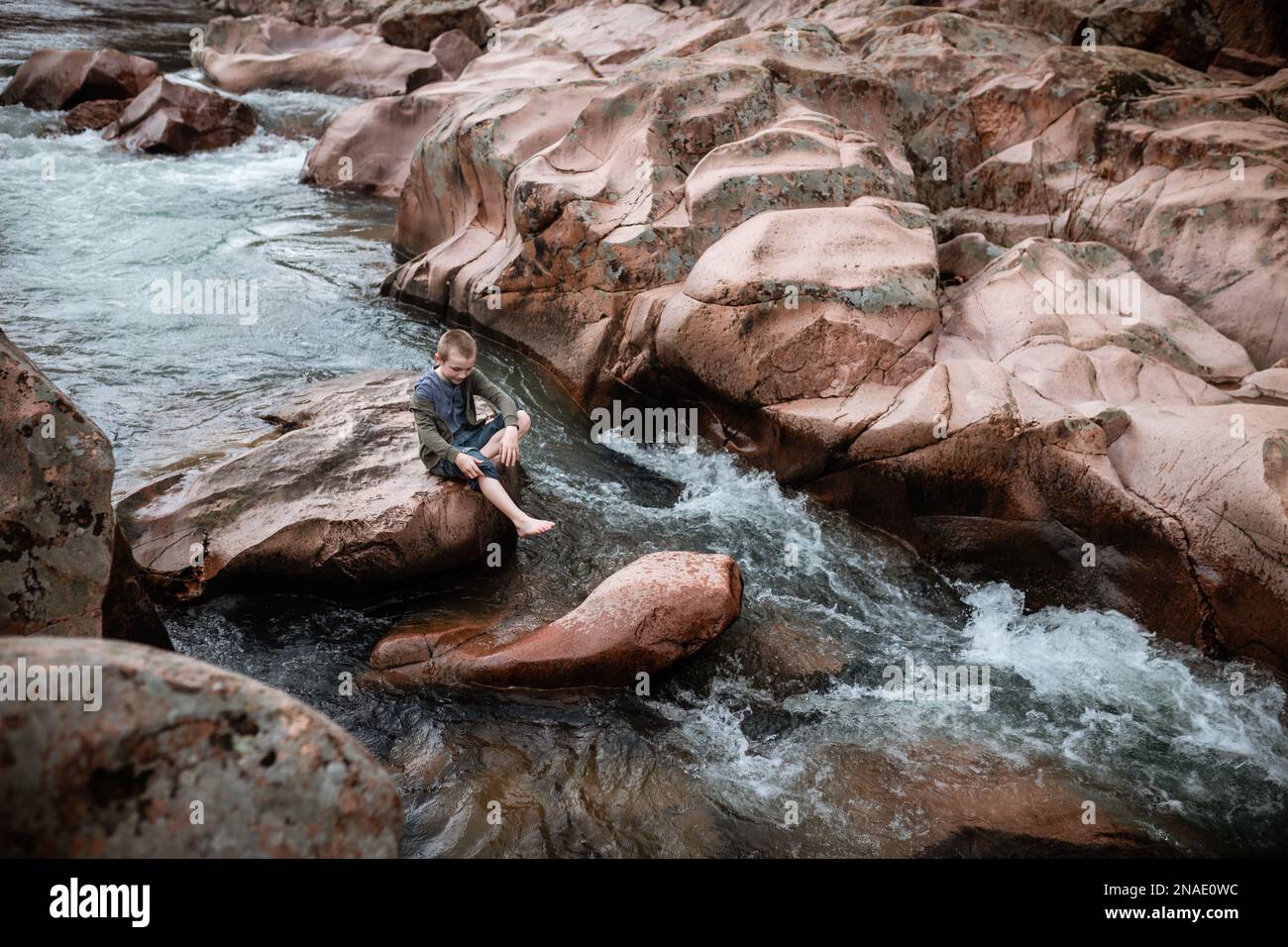 Boy sitting on rock in river along a waterfall Stock Photo - Alamy