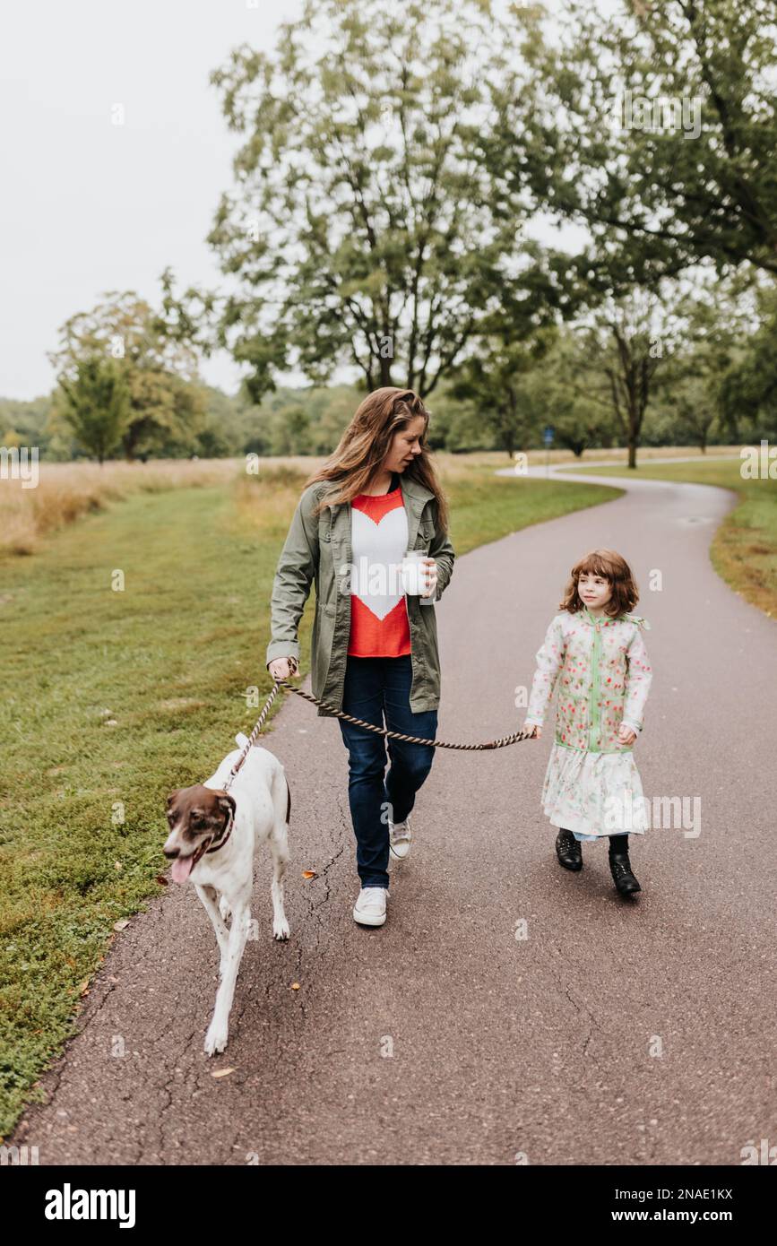A mother and daughters walk their family dog along walking path Stock