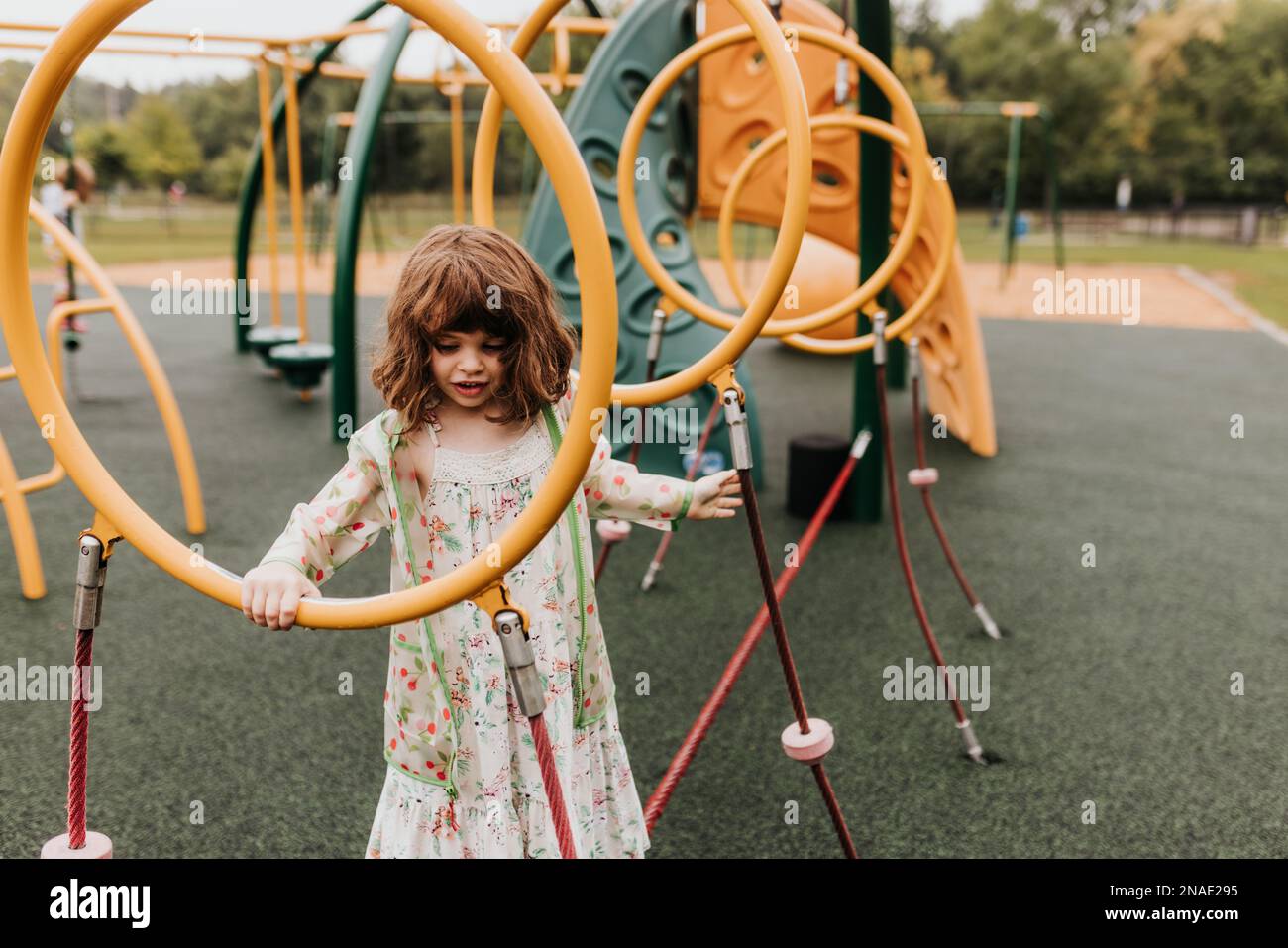 Young girl plays on playground equipment at park on cloudy day Stock Photo