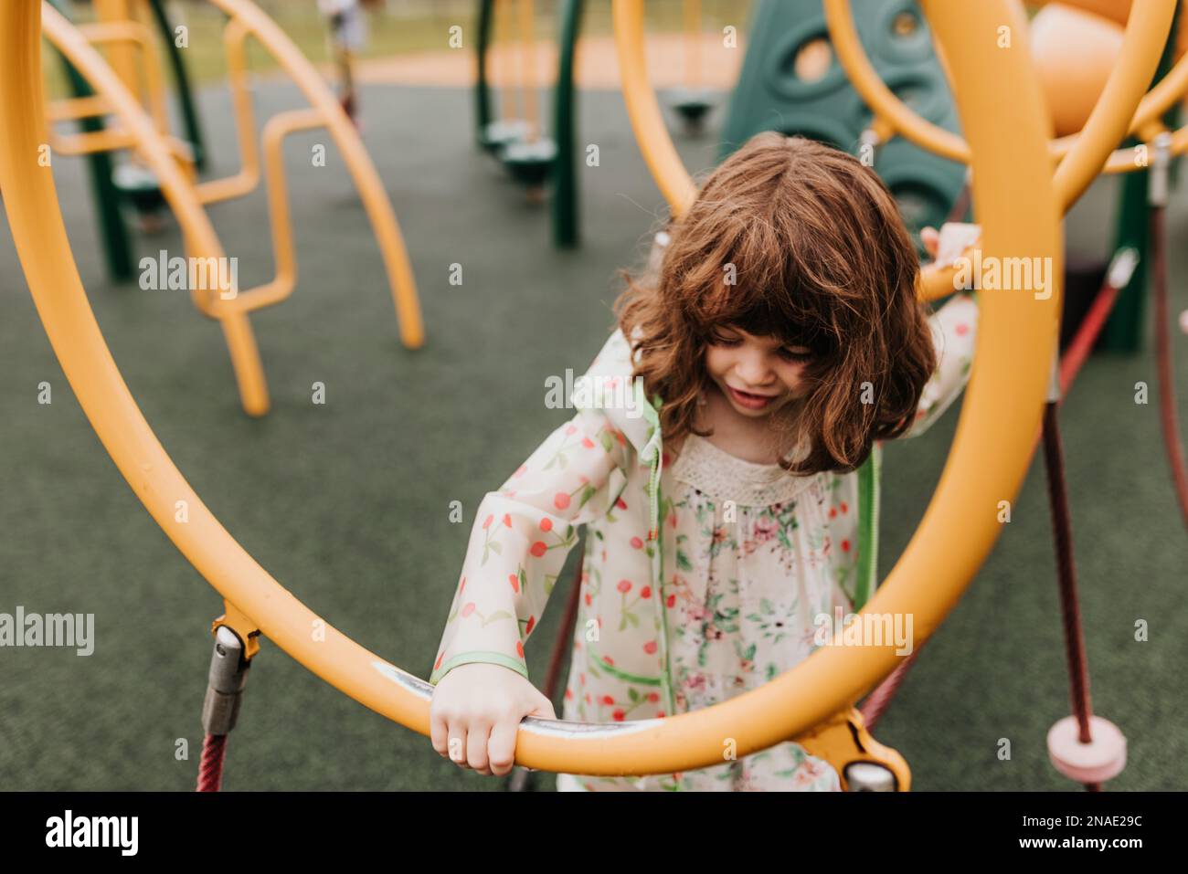 Young girl plays on playground equipment at park on cloudy day Stock Photo