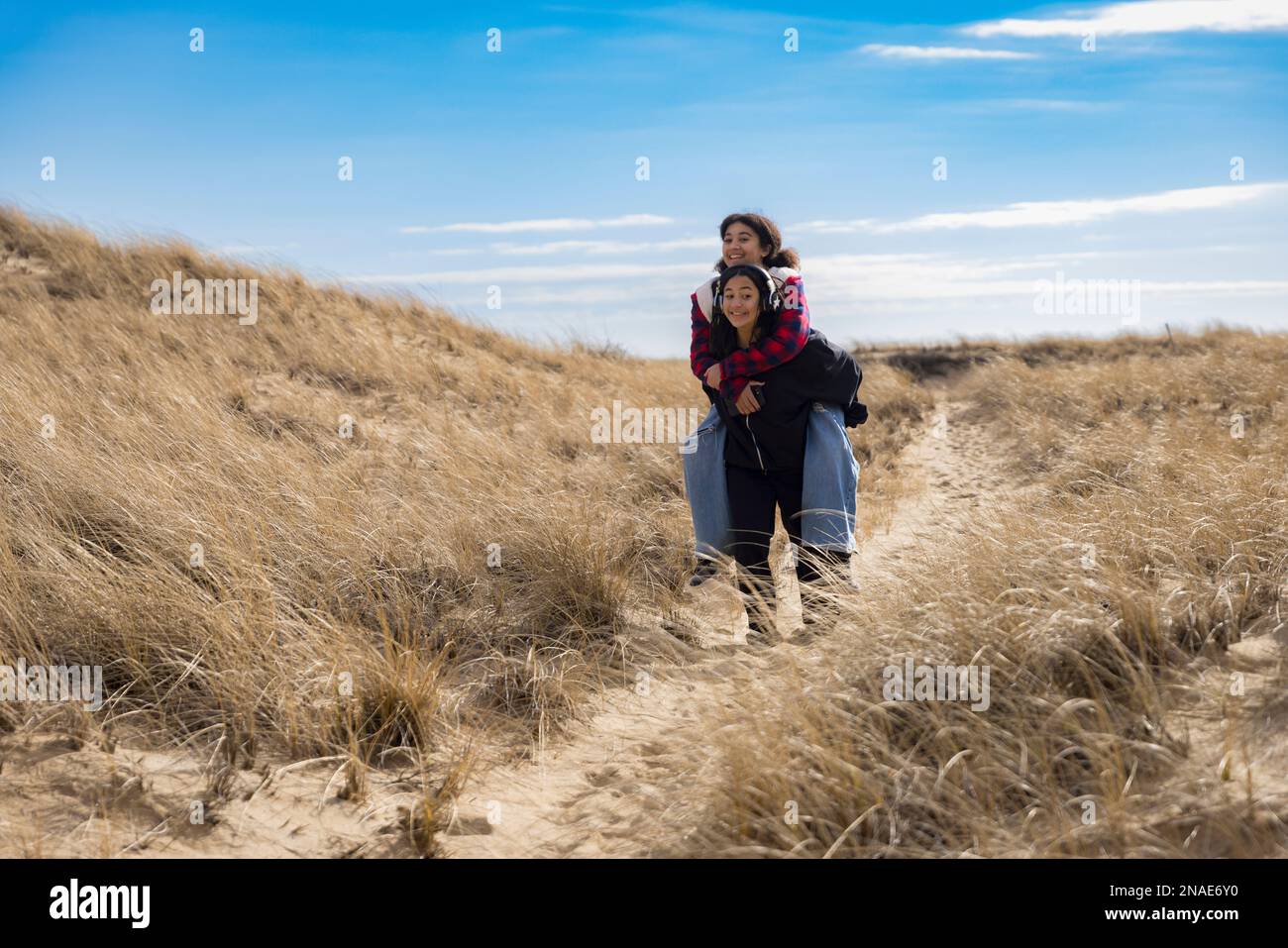 biracial teen sisters piggy-back riding and smiling on sandy path Stock Photo