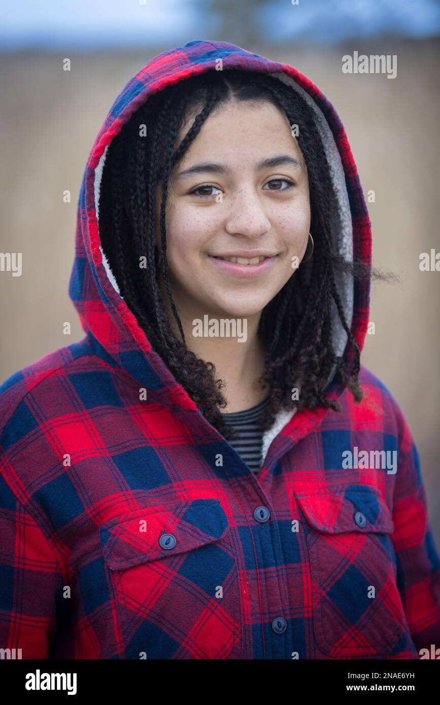 portrait of biracial young woman smiling with braids and hood Stock Photo