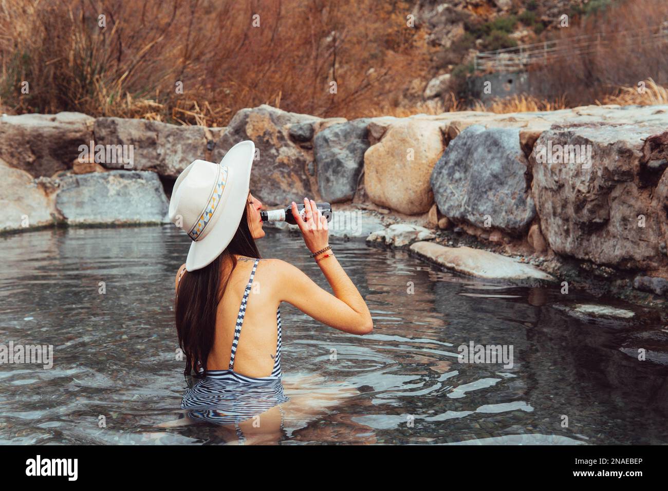 portrait of woman in hat drinking beer in natural hot springs Stock Photo