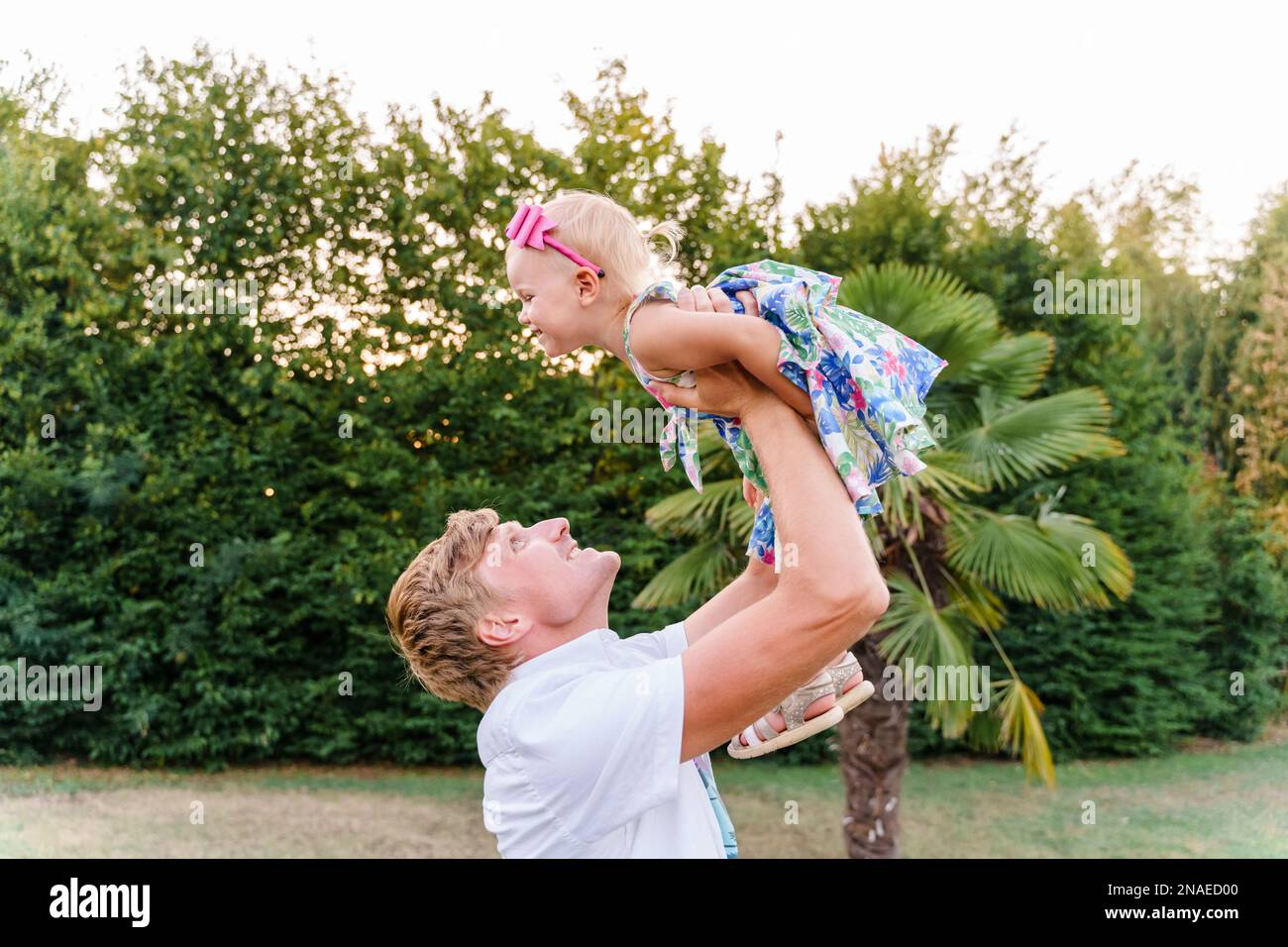 Dad throws his baby girl in his arms in the summer outdoors Stock Photo