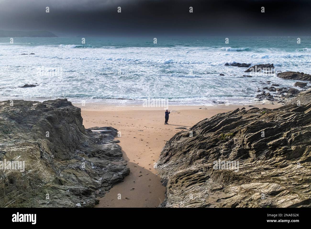 UK weather. A lone person standing on the beach at the secluded Little Fistral with Storm Claudio approaching the coast over Newquay Bay in Cornwall i Stock Photo