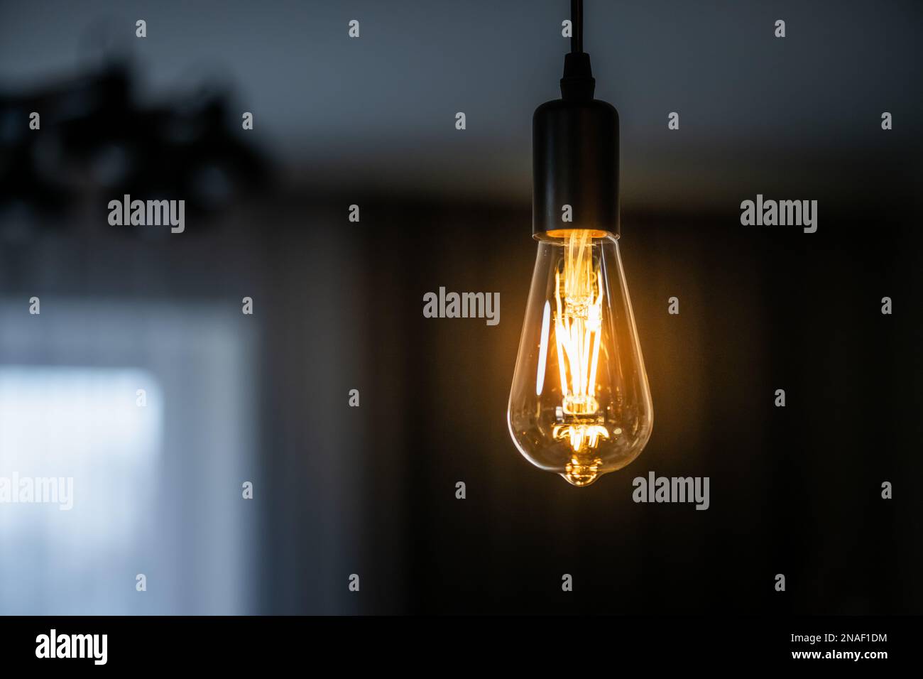 Vintage hanging Edison light bulb with warm light over dark home background Stock Photo