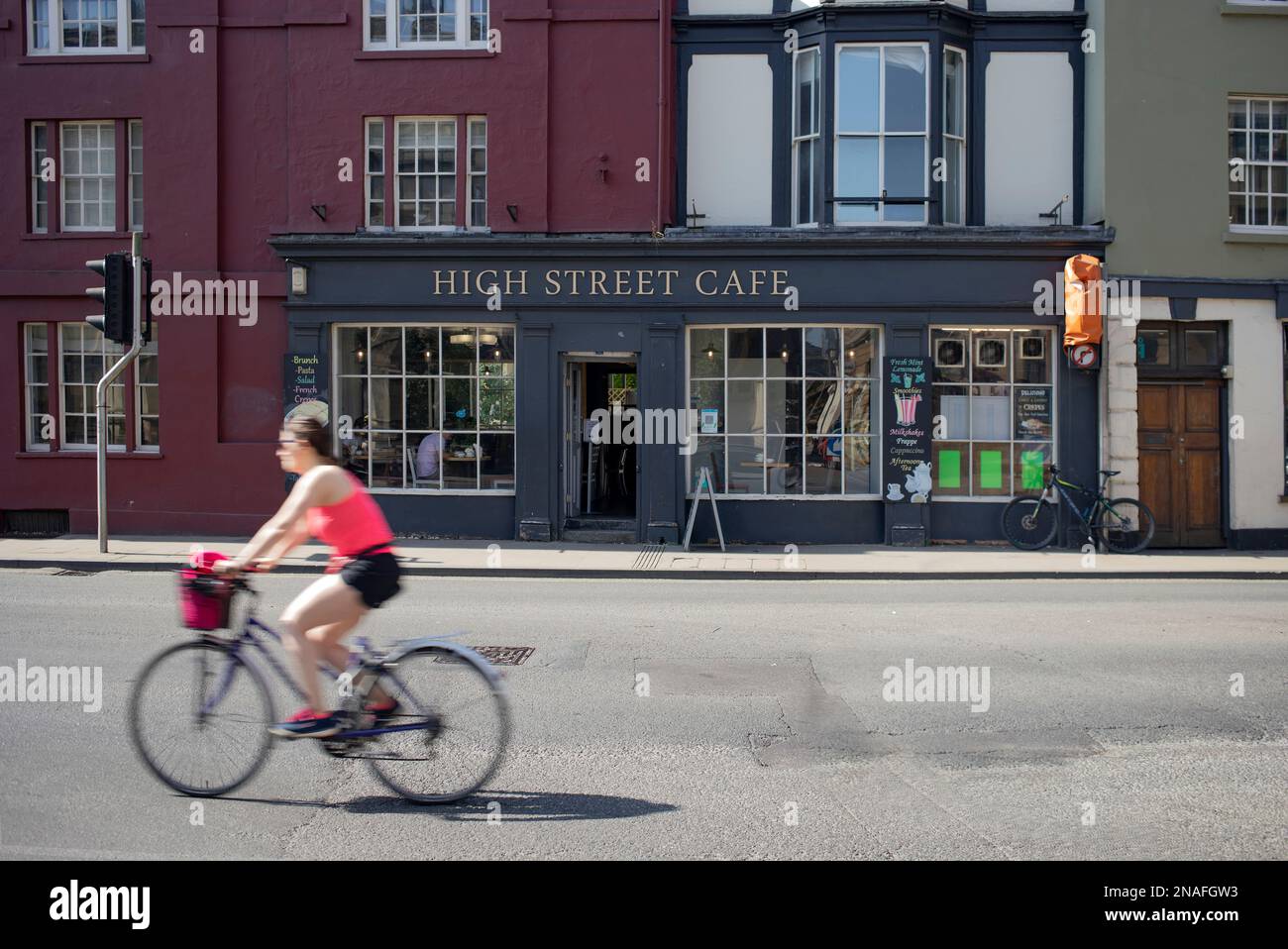 Cyclist rides by a cafe along a street in Oxford, UK; Oxford, England Stock Photo