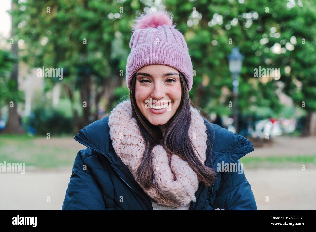 Close up portrait of caucasian young woman smiling and looking at camera. Front view of happy teenage brunette girl with autumn clothes, hat, coat and scarf standing at park outdoors. High quality photo Stock Photo